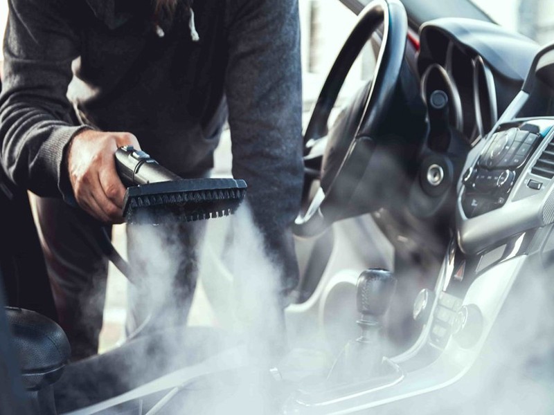 Professional steam cleaning car interior with handheld tool removing mold