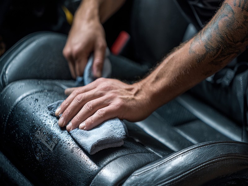 Professional hands cleaning car seat with microfiber cloth for odor removal